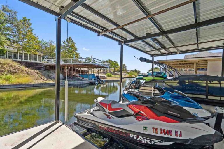 A boat dock with jet skis and a house surrounded by trees and water along Cherokee Creek in Texas